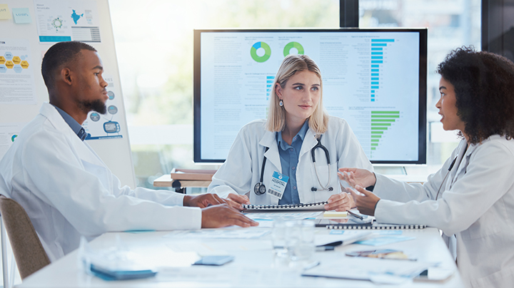 healthcare professionals discussing something in front of screens and posters showing data visualizations