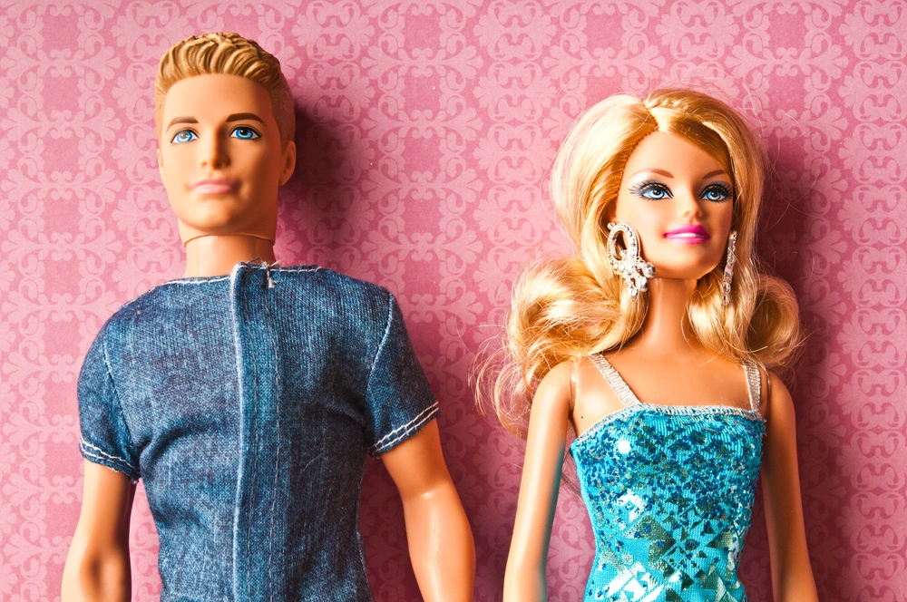 A Ken and Barbie doll, placed in front of a pink background